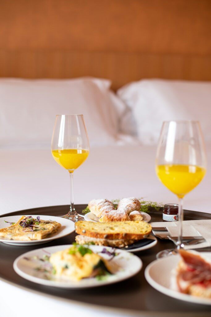 Cozy hotel breakfast buffet featuring fresh pastries, colorful fruit platters, hot coffee, and a stylish bar area with cocktails and wine glasses ready to serve guests.