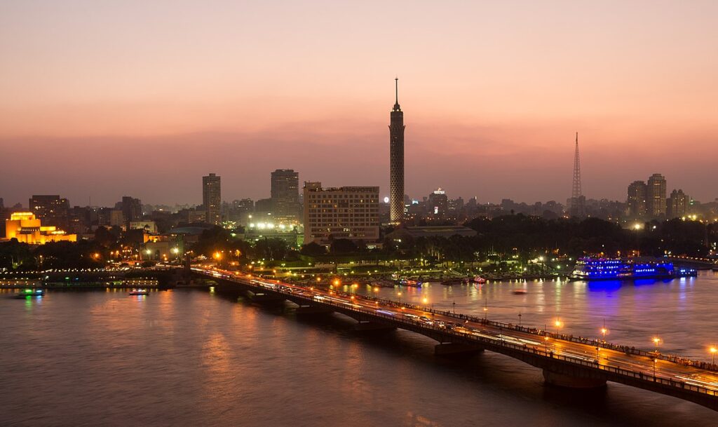 A scenic view of Cairo at sunset with the Nile in the foreground and city skyline in the background, capturing the vibrant energy of the city for an Egypt travel guide