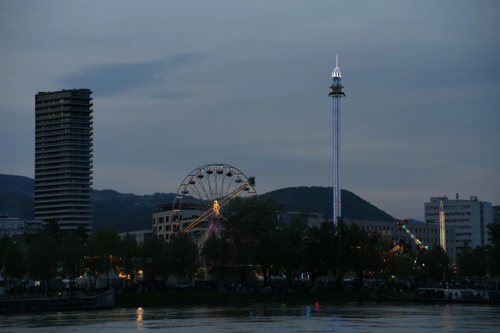 A scenic view of Linz with the Danube River, historic buildings, and Pöstlingberg hill at sunset