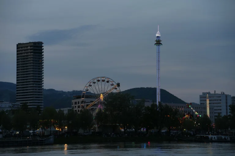 A scenic view of Linz with the Danube River, historic buildings, and Pöstlingberg hill at sunset