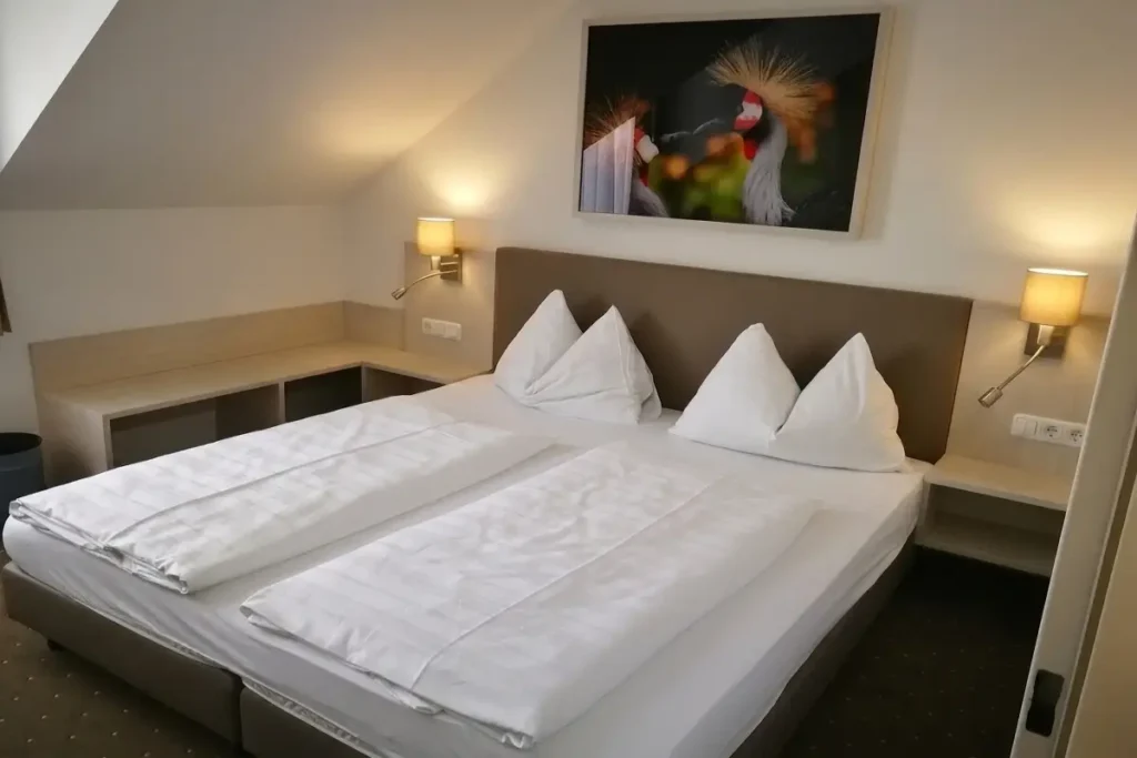 A tidy guest room at Hotel Lokomotive featuring a double bed under a sloped ceiling, light wood built-in nightstands, and a framed picture of birds above the brown headboard